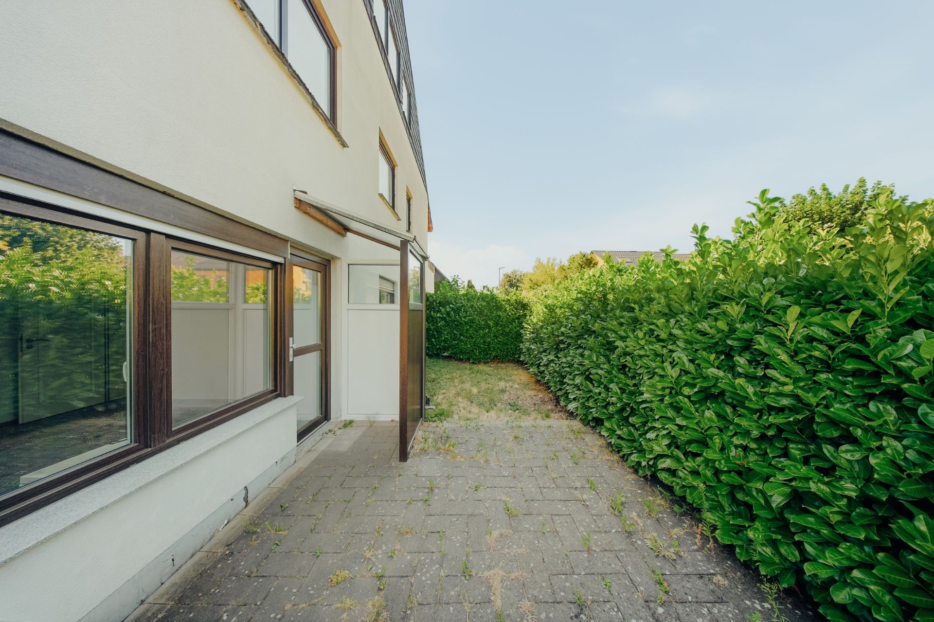 Gepflasterte Terrasse an einem Wohnhaus mit Hecke und kleinen Grünflächen.