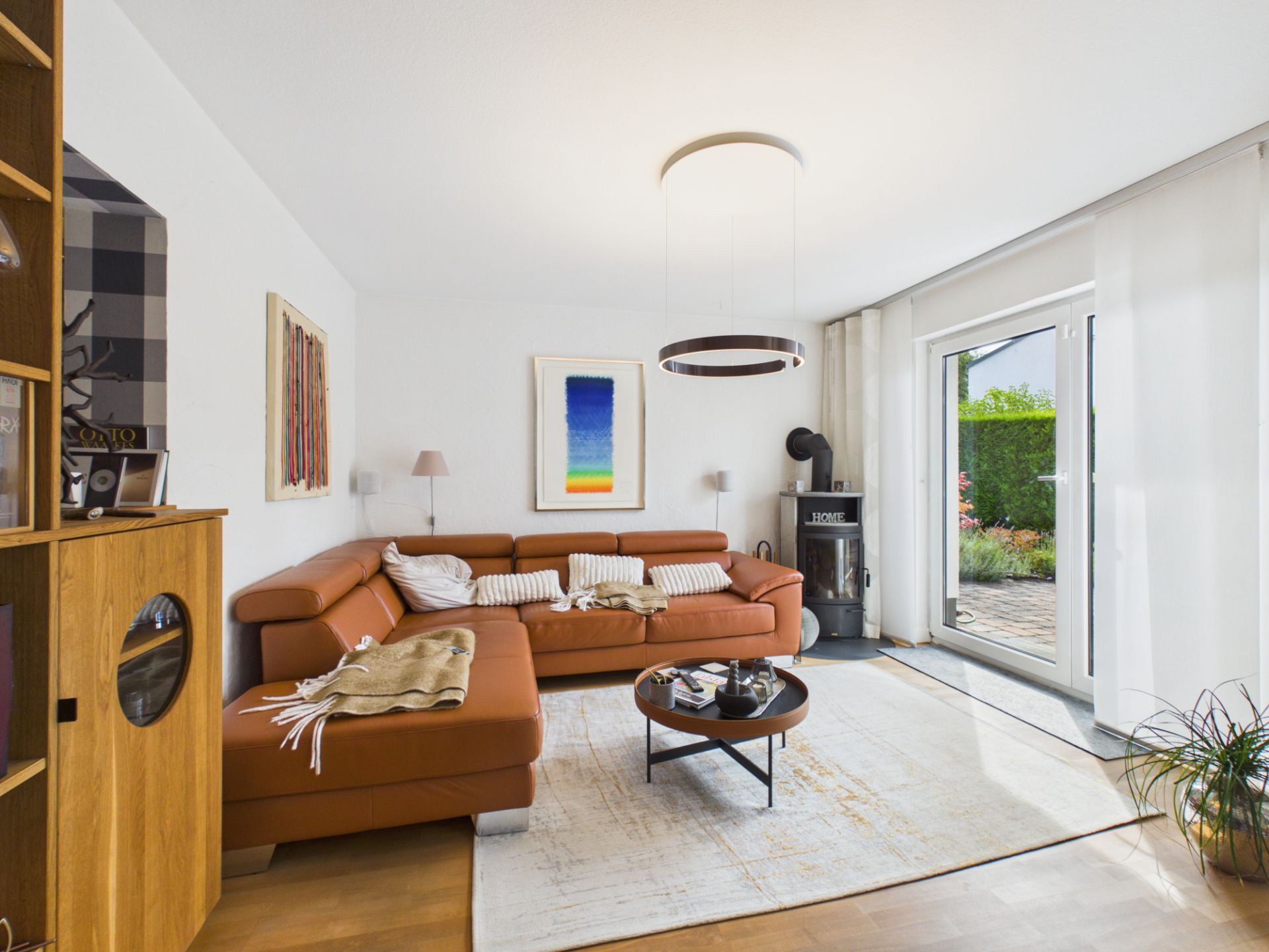 Modernes Wohnzimmer mit braunem Ecksofa, Couchtisch, Kaminofen und Zugang zur Terrasse.