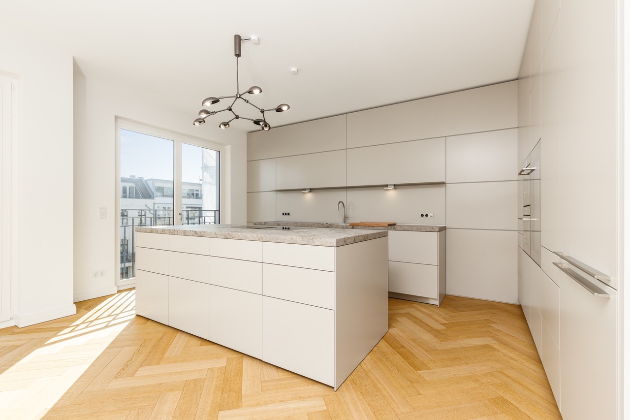 Moderne, helle Einbauküche mit Kücheninsel und großem Fenster auf Parkettboden.
