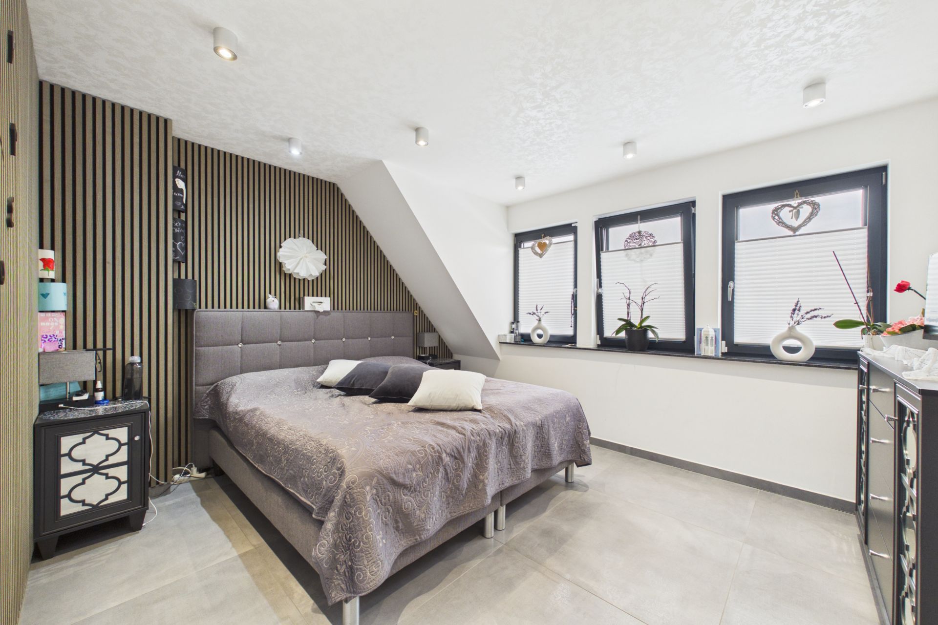 Modernes Schlafzimmer mit großem Bett, drei Fenstern und dekorierten Nachttischen.