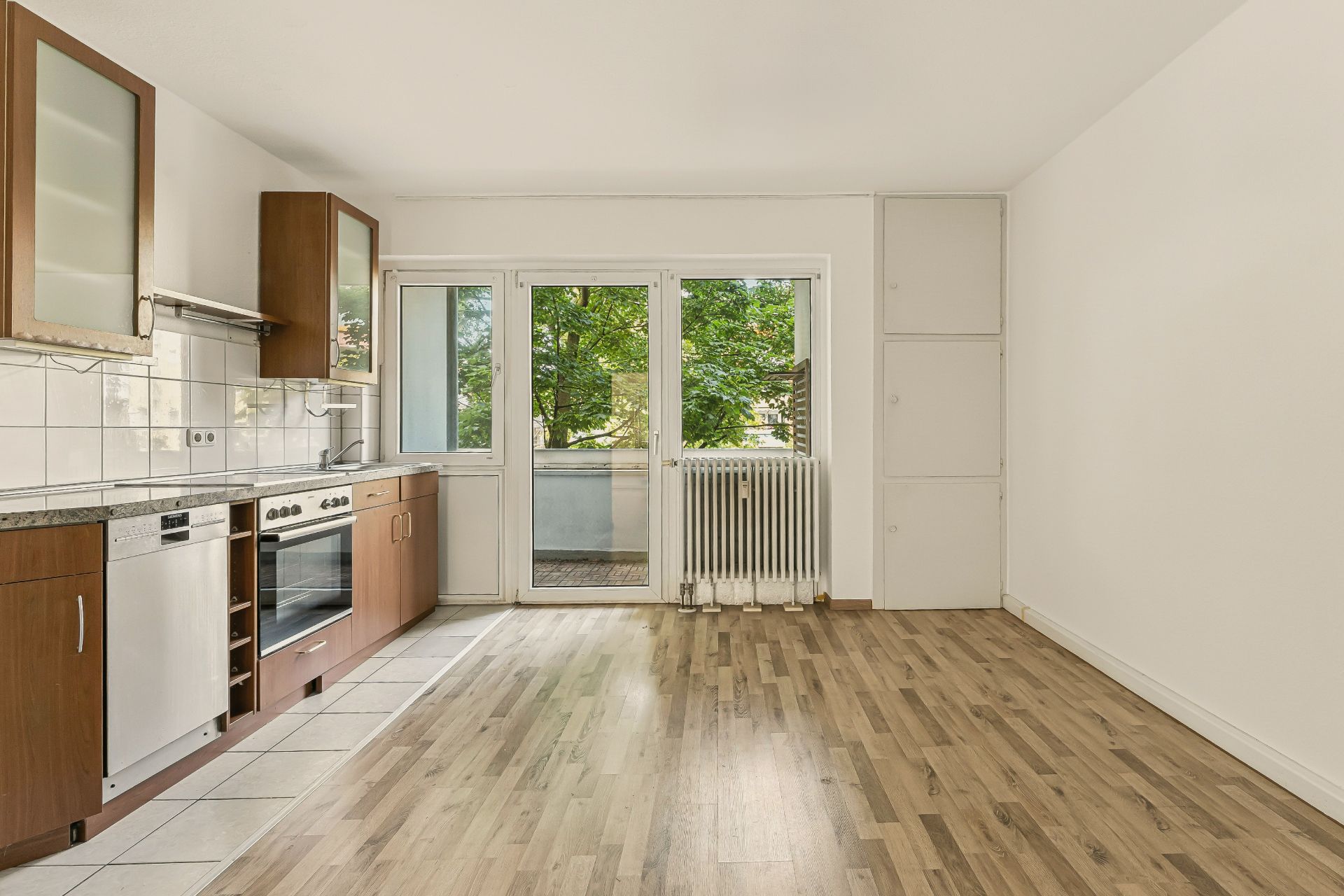 Helle Küche mit Holzboden, Einbauküche und Zugang zu einem Balkon mit Blick ins Grüne.