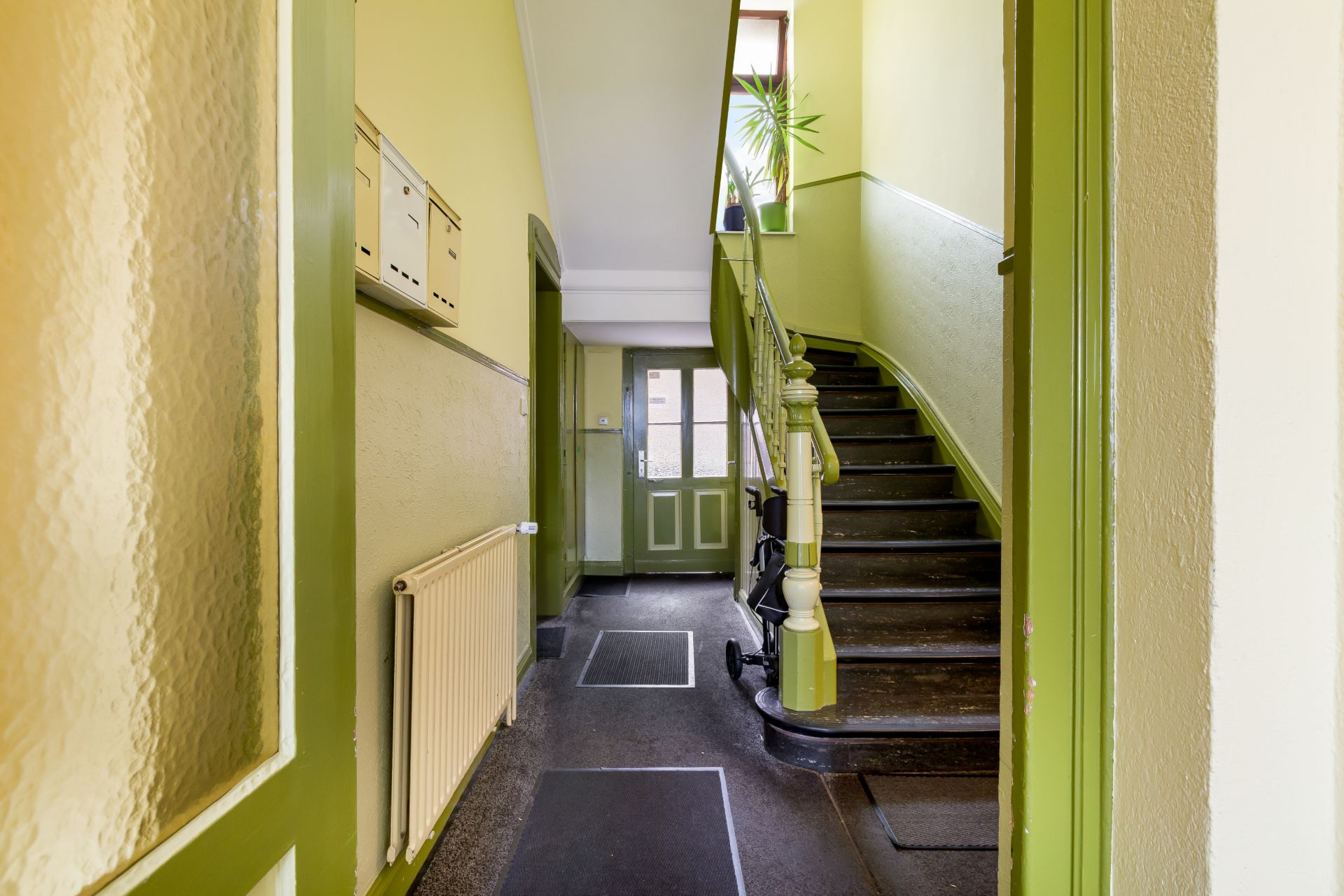 Hausflur mit Treppenaufgang, Briefkästen, Heizkörper und Kinderwagen an der Wand.