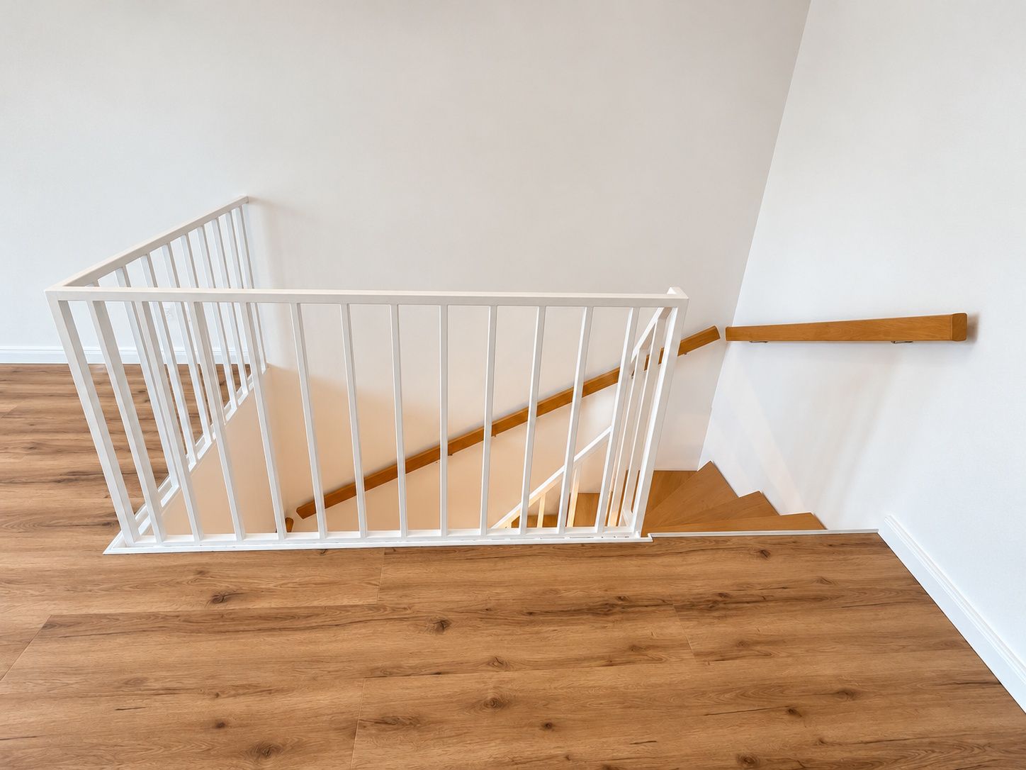 Holztreppe mit weißem Geländer und Handlauf an einer weißen Wand.