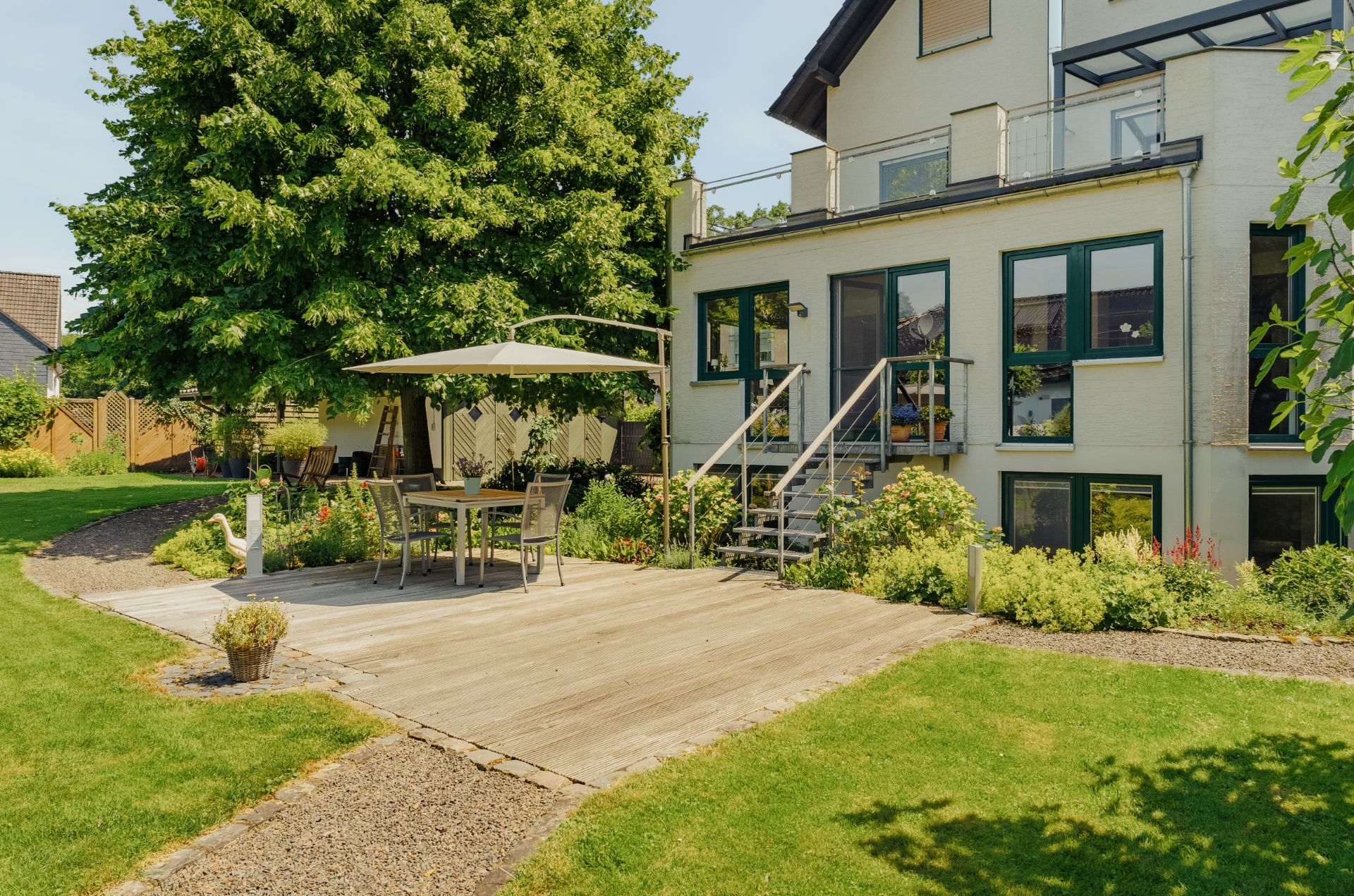 Terrasse mit Sitzgruppe und Sonnenschirm im Garten eines Wohnhauses.
