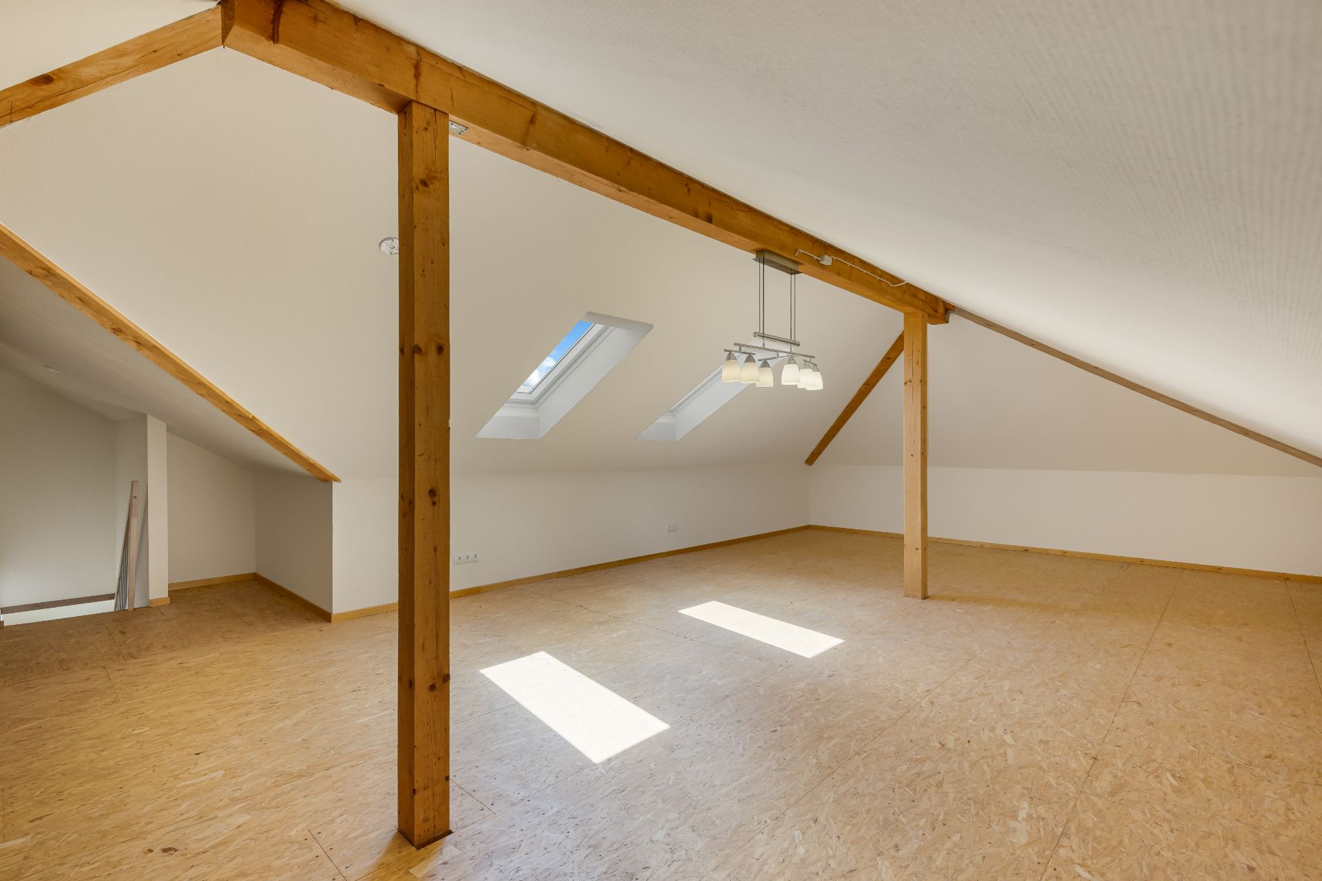 Heller Dachbodenraum mit Dachfenstern, Holzbalken und heller Holzdecke.