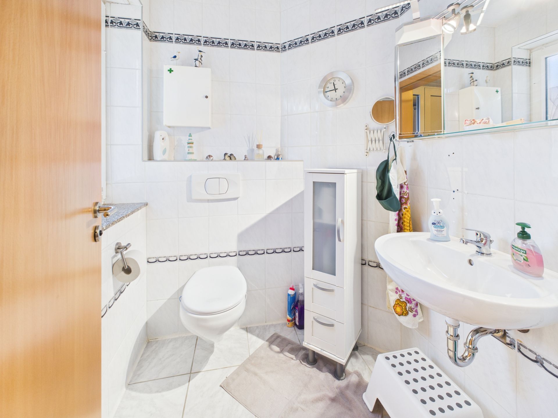 Helles Badezimmer mit WC, Waschbecken, Spiegelschrank und kleinem weißen Schrank.