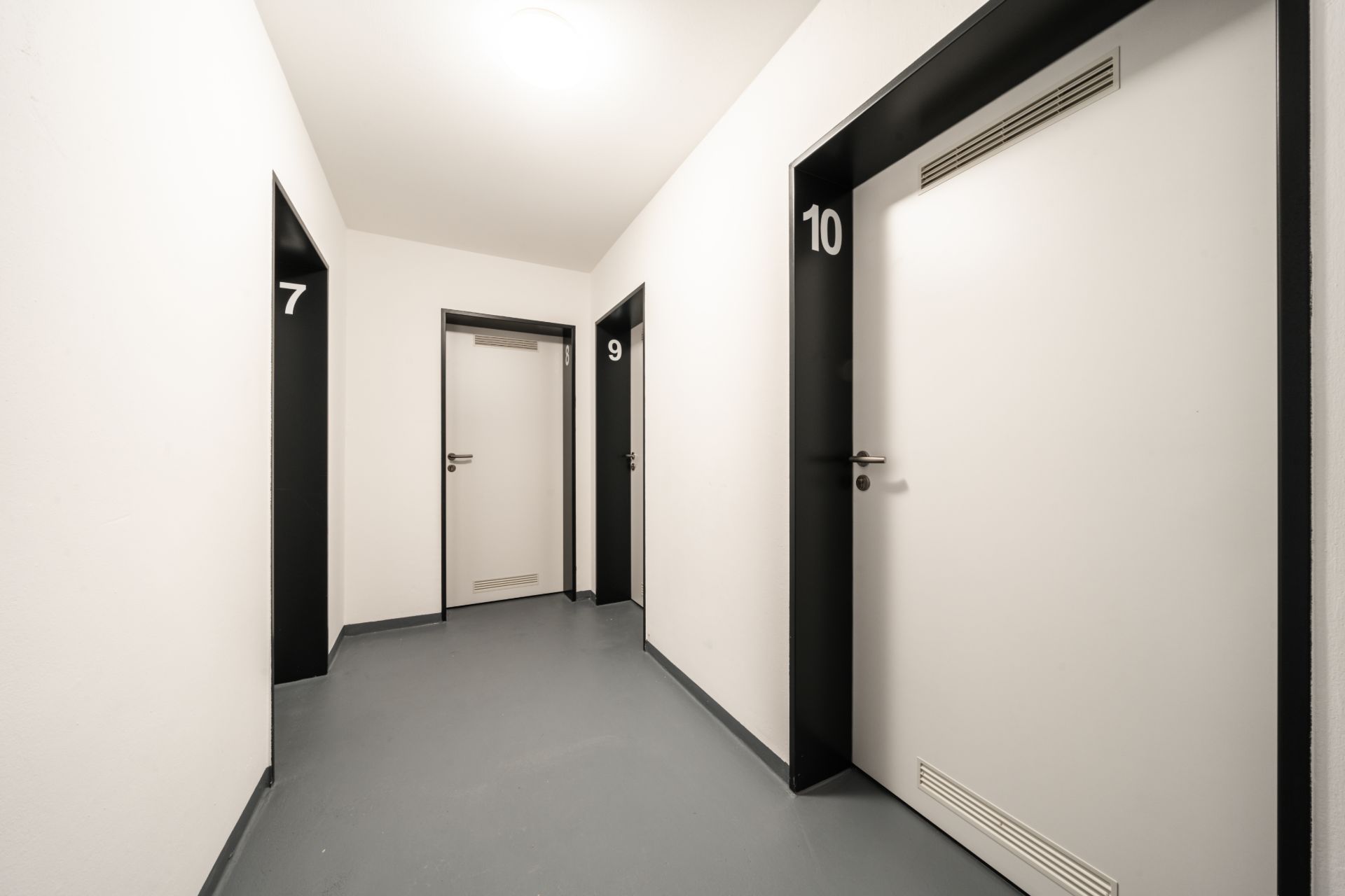 Ein heller Flur mit vier weißen Türen, nummeriert 7, 9 und 10.