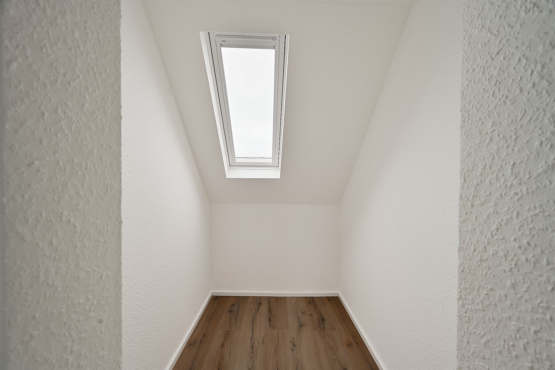 Kleiner leerer Raum mit weiß gestrichenen Wänden, Dachfenster und Holzfußboden.