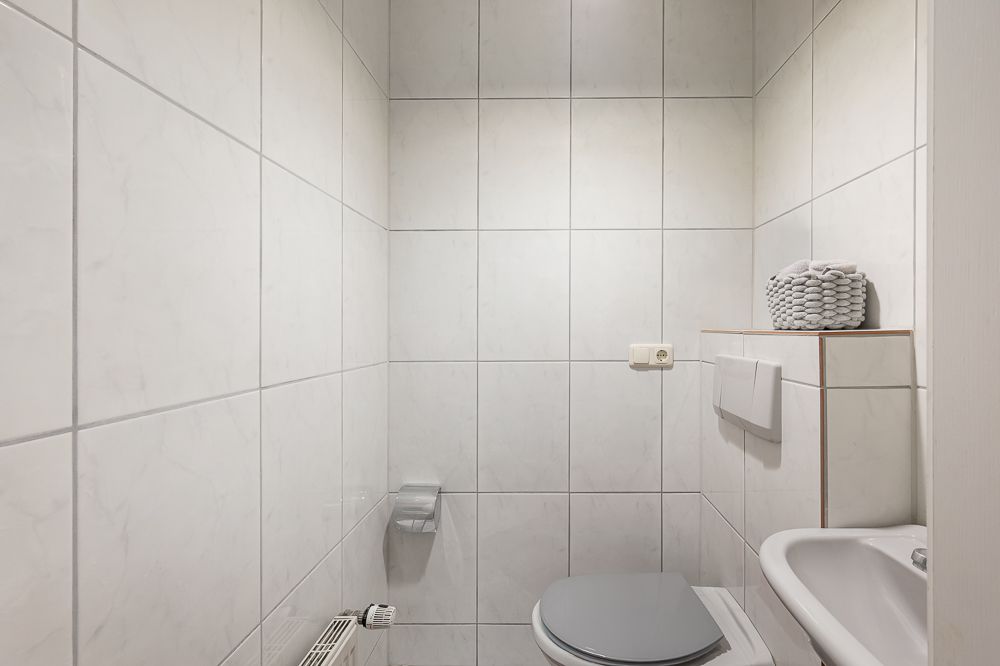 Kleines, gefliestes Badezimmer mit Toilette, Waschbecken und grauem Klodeckel.
