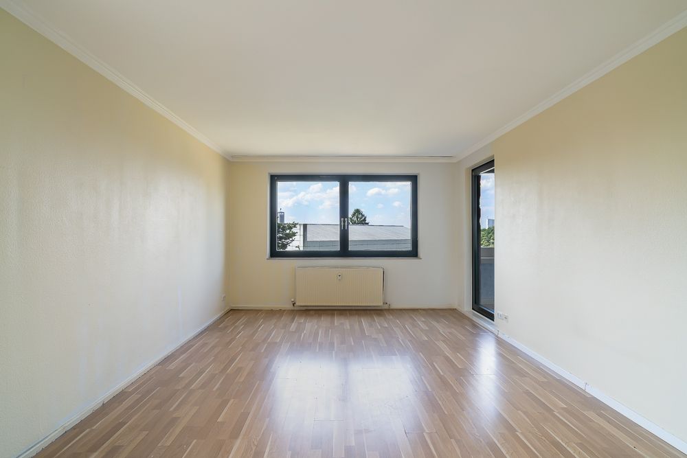 Helles, leeres Zimmer mit Holzfußboden, zwei Fenstern und Heizkörper unter dem Hauptfenster.
