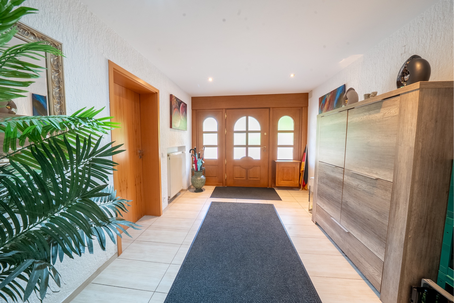 Heller Flur mit Holztür, Teppichläufer, Schrank, Pflanzen und Wanddekoration.