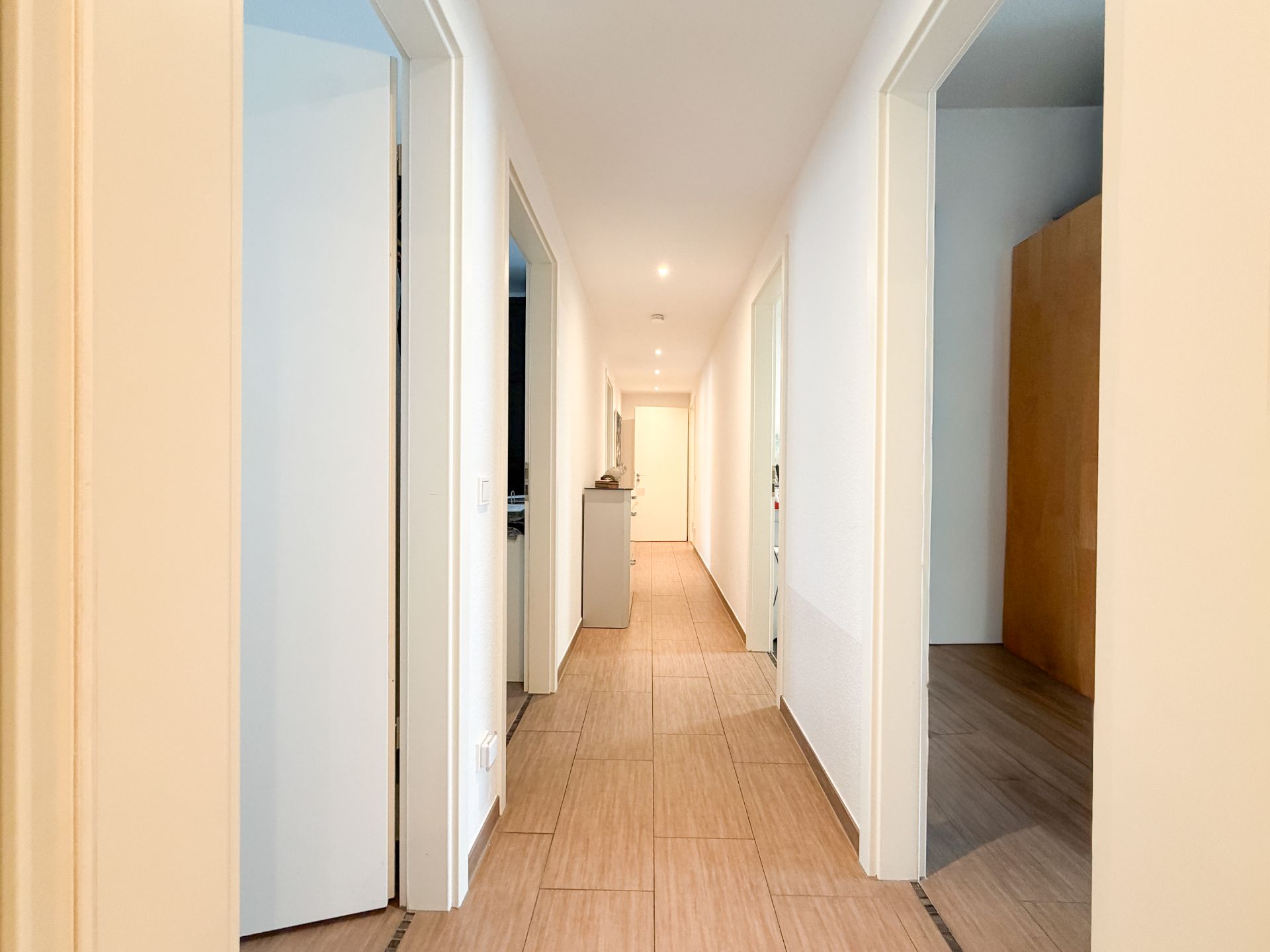 Heller Flur mit mehreren offenen Türen und Holzfußboden in einer Wohnung.