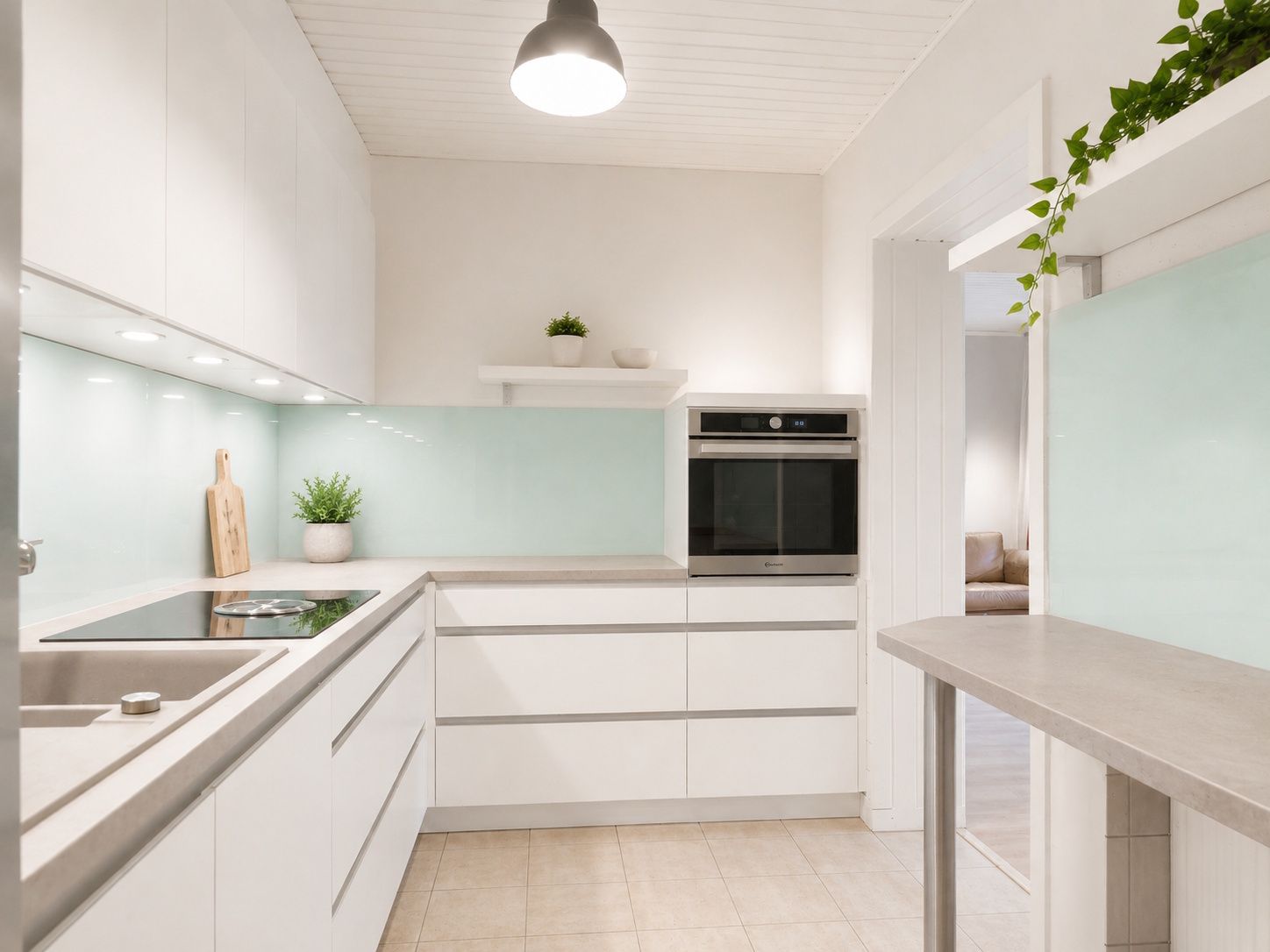 Moderne, helle Küche mit weißen Schränken, Pflanzen und eingebautem Ofen.