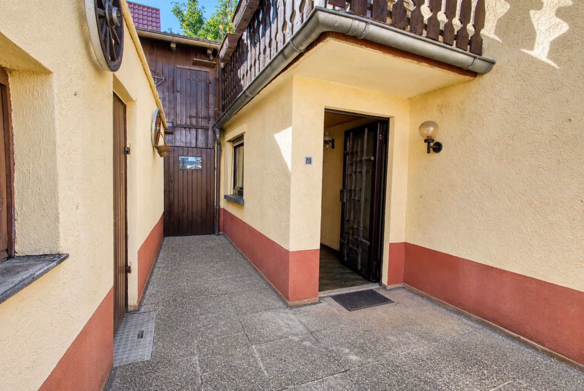 Hof eines Wohnhauses mit gelber Fassade, offenem Eingang und kleinem Balkon.