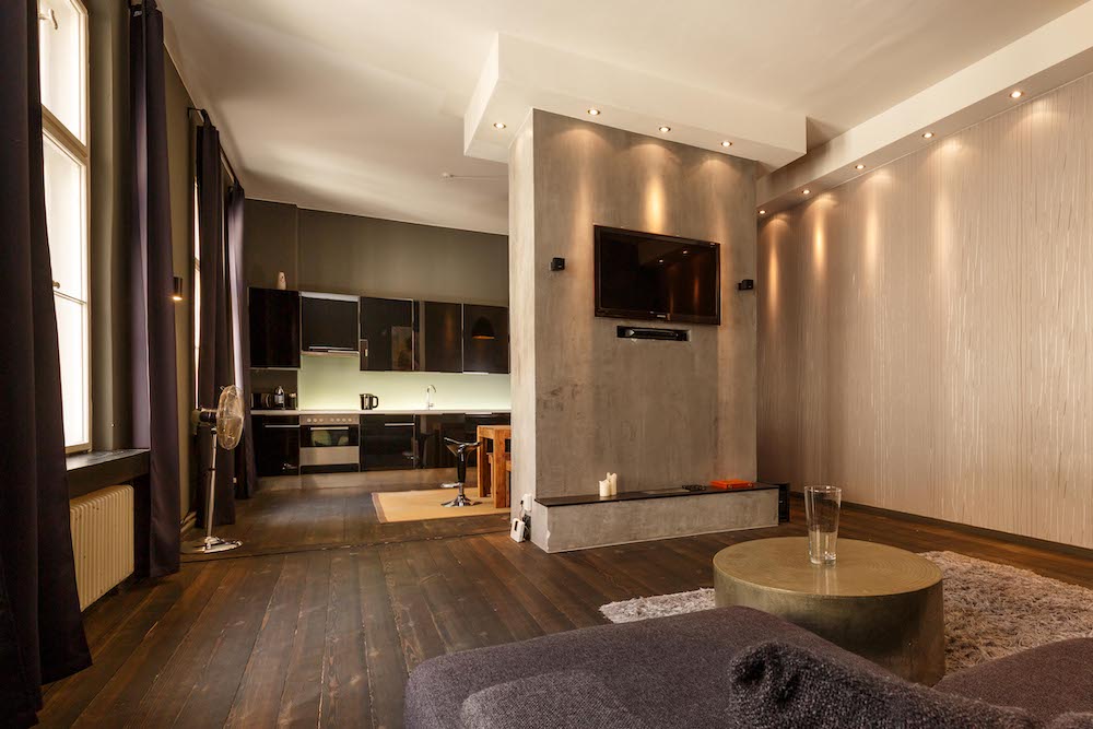 Modernes Wohnzimmer mit Fernseher, Teppich und offener Küche im Hintergrund.