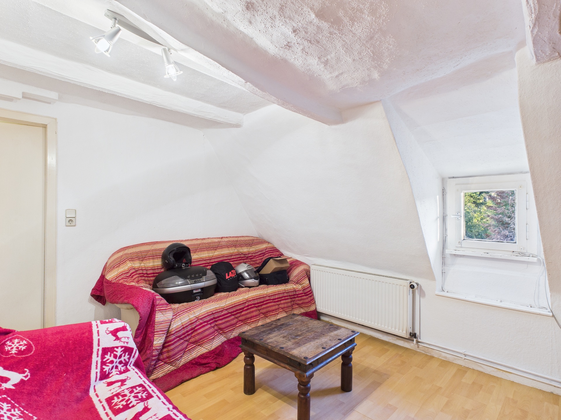 Kleines Zimmer mit Dachschräge, Sofa, kleinem Tisch und Fenster mit Blick ins Grüne.