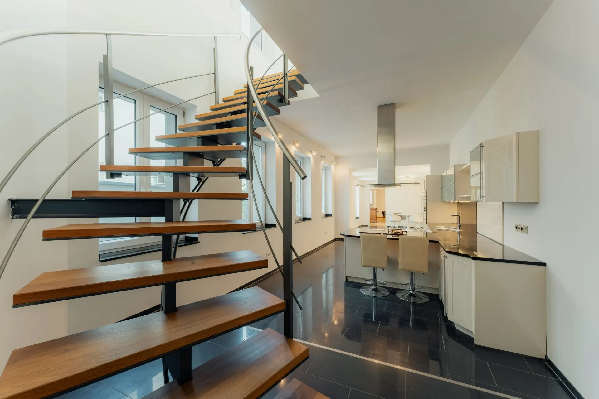 Offene Holztreppe und moderne Küche mit hellen Möbeln in einem Wohnraum.