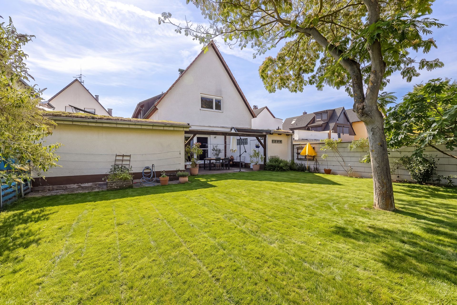 Großer Garten mit grünem Rasen, Baum und Terrasse hinter einem Wohnhaus.
