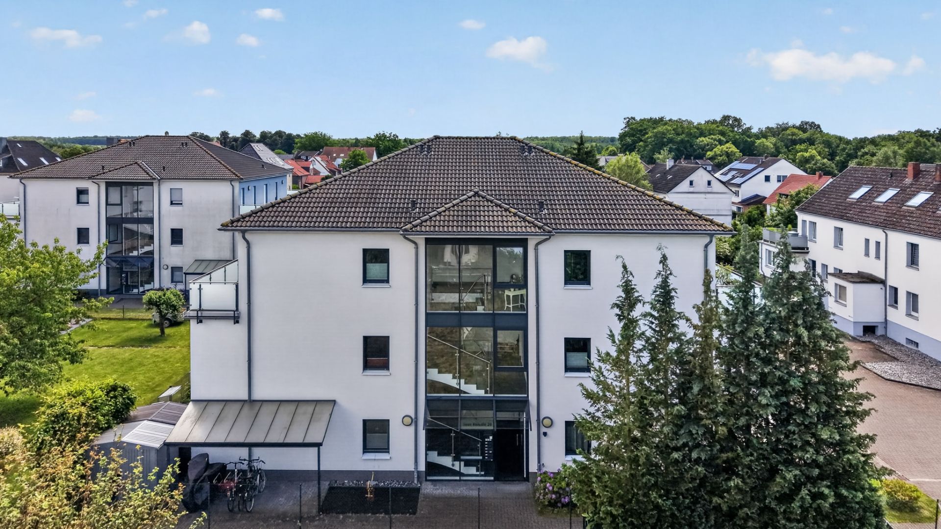 Modernes Mehrfamilienhaus mit Glasaufgang und Fahrradstellplatz vor dem Gebäude.