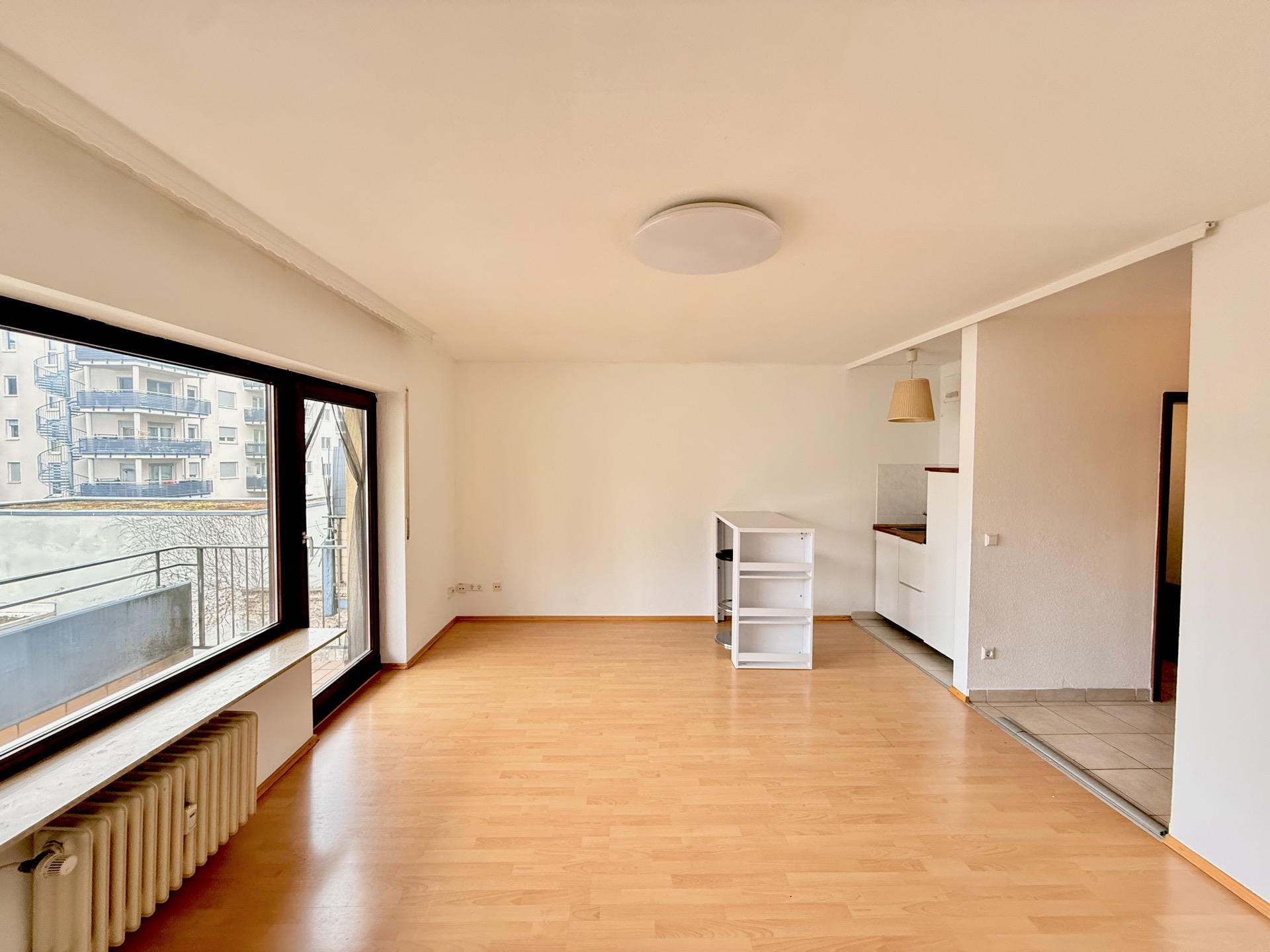 Helles Wohnzimmer mit Parkettboden, großem Fenster und Zugang zur offenen Küche.