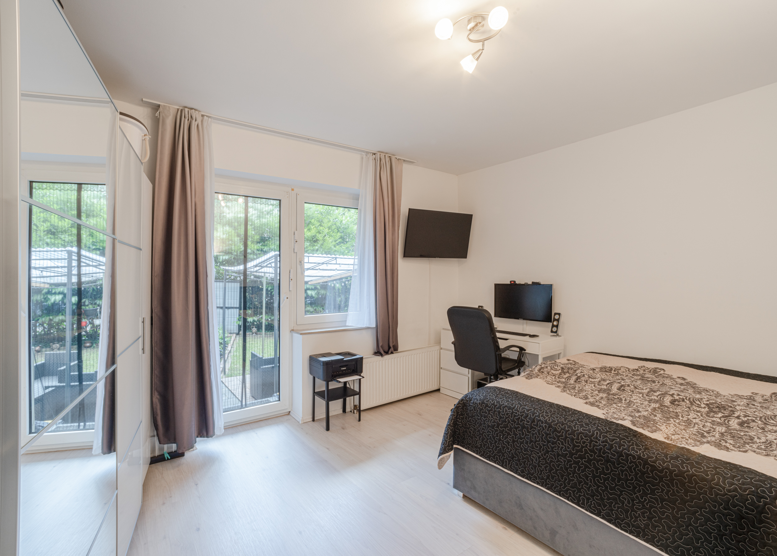 Modernes Schlafzimmer mit Schreibtisch, Bett und Zugang zu einer Terrasse mit Gartenblick.