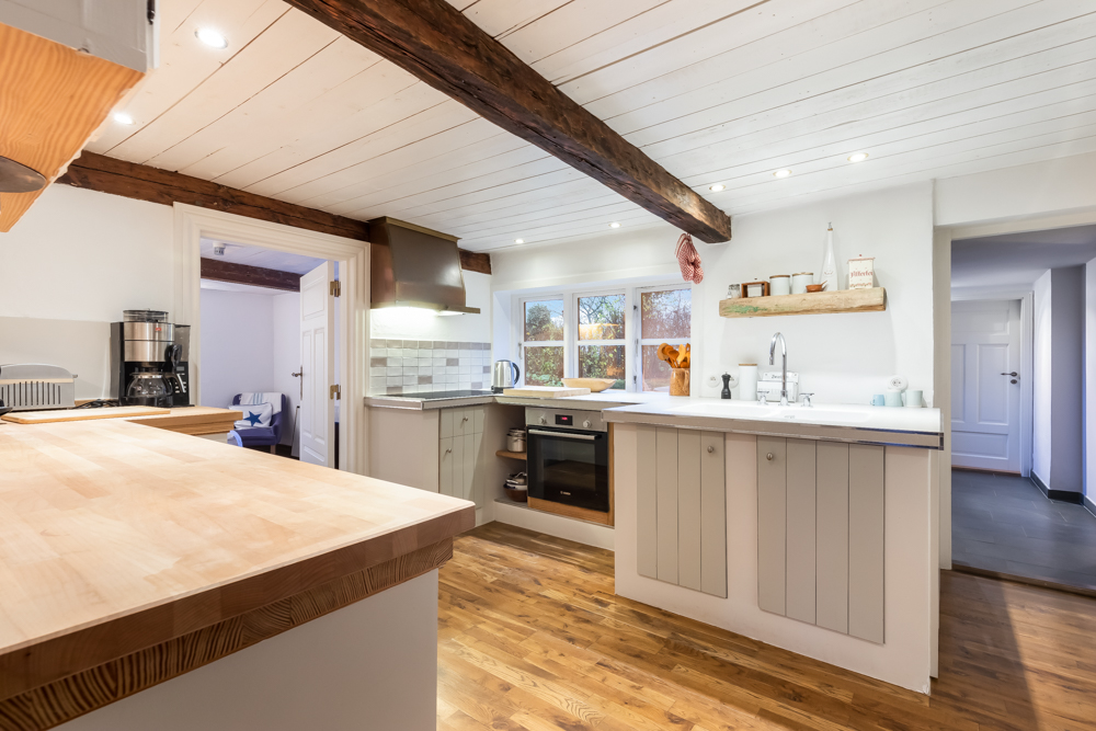 Helle, moderne Küche mit Holzdetails, weißen Wänden und sichtbaren Holzbalken an der Decke.