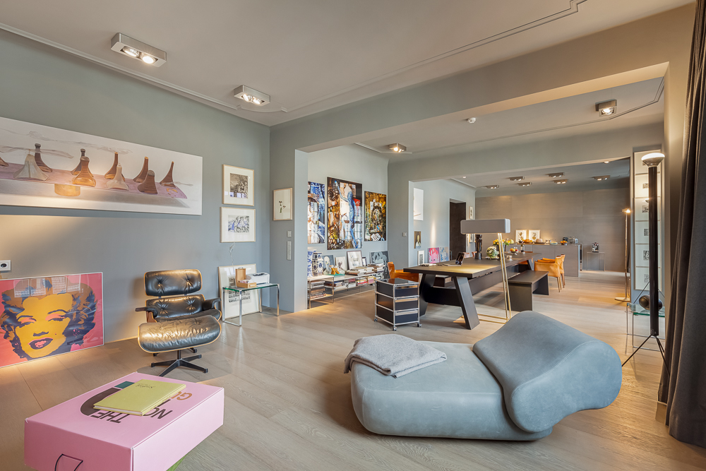 Modernes Wohnzimmer mit Kunstwerken, grauem Sessel, Designtisch und Parkettboden.