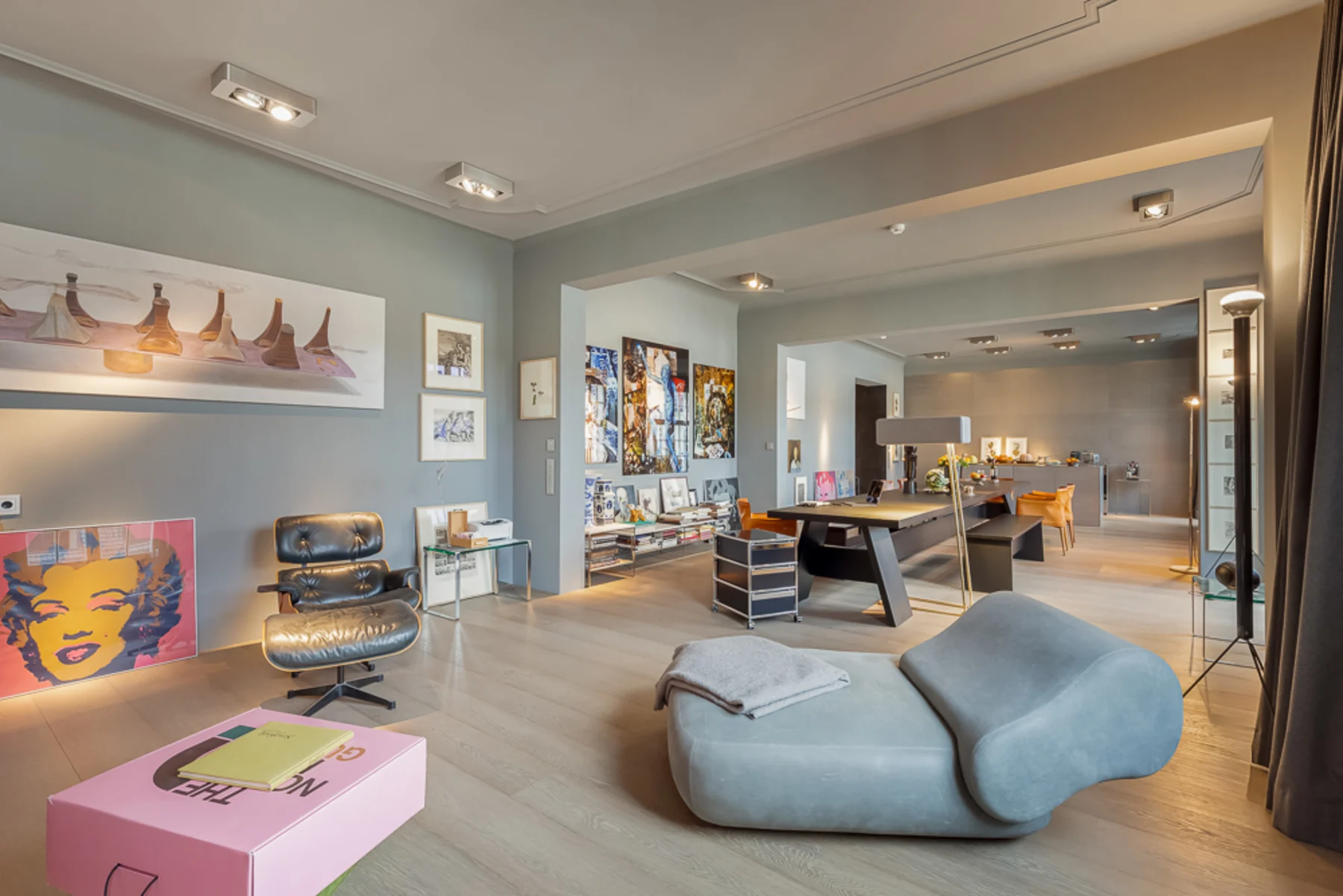Modernes Wohnzimmer mit Kunstwerken, grauem Sessel, Designtisch und Parkettboden.