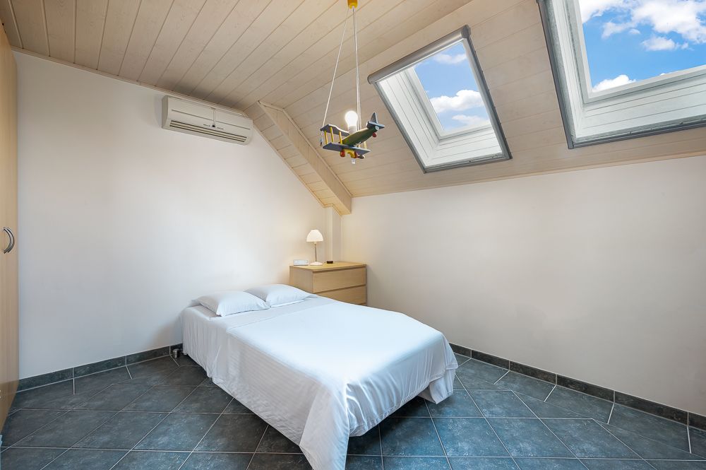 Helles Schlafzimmer mit Doppelbett, Dachfenstern, Nachttisch und Flugzeuglampe.