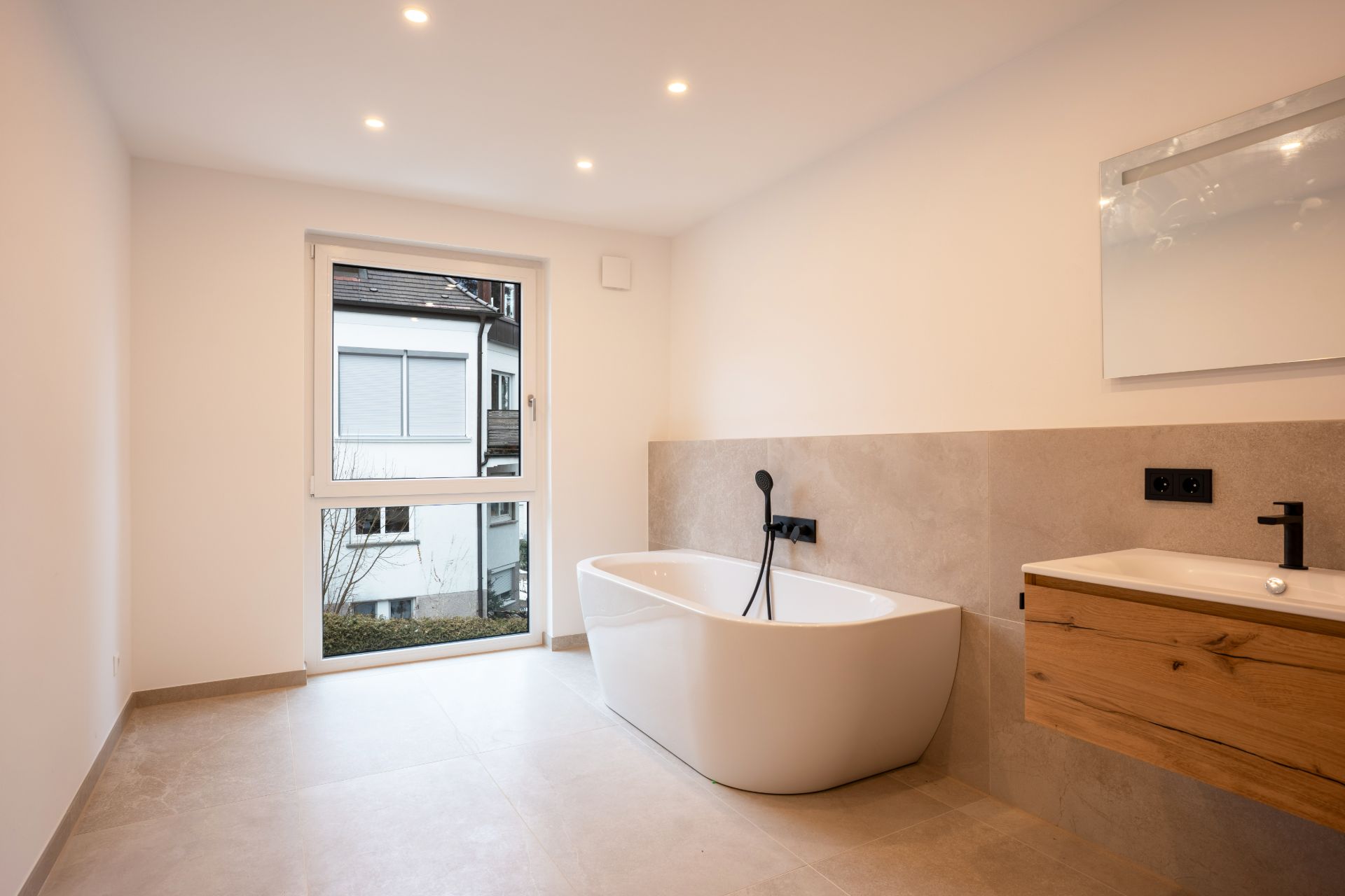 Modernes Badezimmer mit freistehender Badewanne, großem Fenster und Holzwaschtisch.
