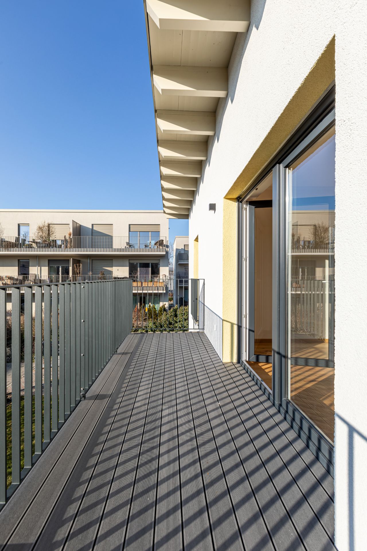 Moderner Balkon mit Geländer, angrenzend an ein Wohngebäude, bei klarem Himmel.
