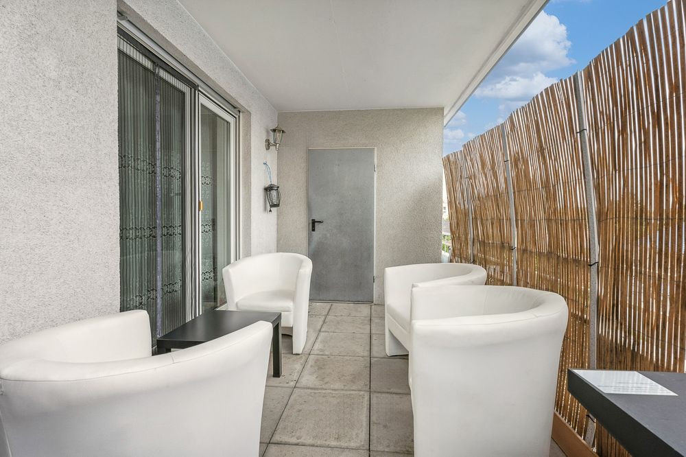 Überdachter Balkon mit vier weißen Sesseln, kleinem Tisch und Bambus Sichtschutz.