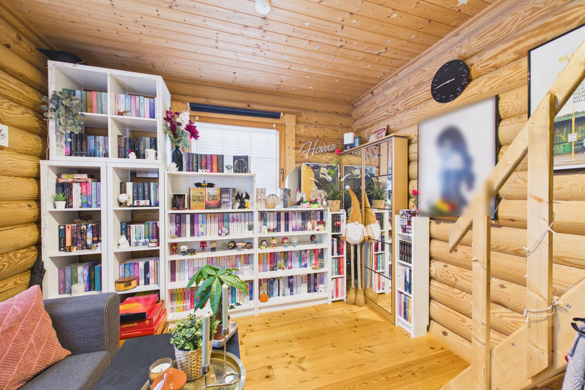 Gemütliches Wohnzimmer mit Holzverkleidung, vielen Bücherregalen und Pflanzen.