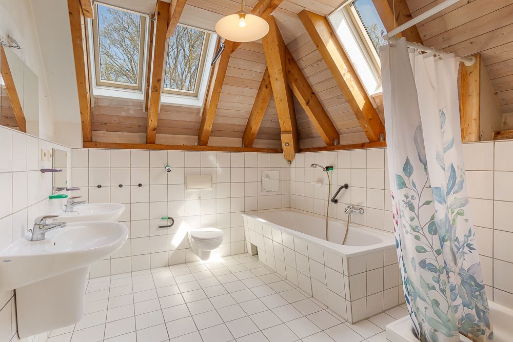 Helles Badezimmer mit Dachschrägen, Dachfenstern, zwei Waschbecken, Badewanne und Duschvorhang.