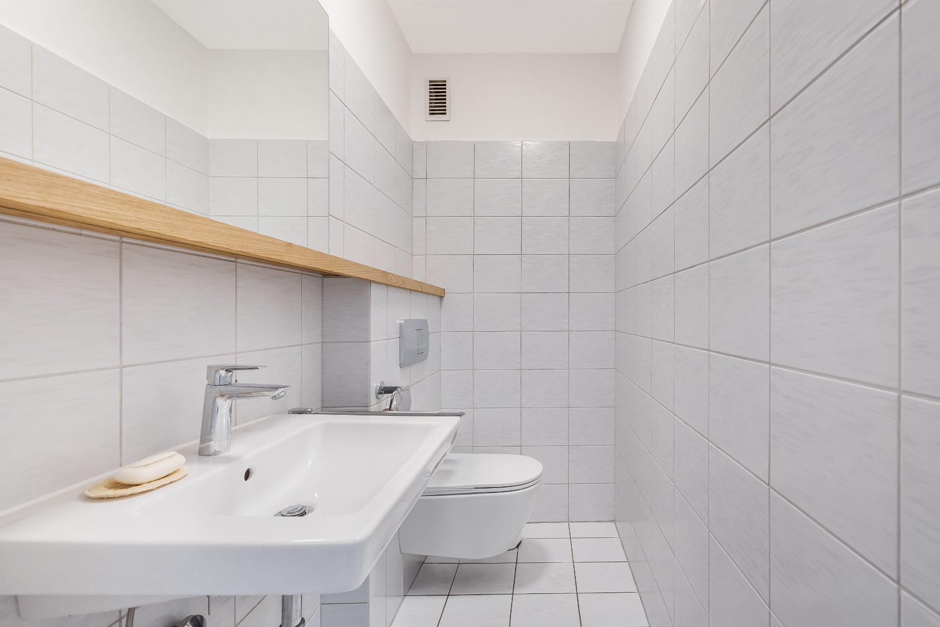 Helles, gefliestes Badezimmer mit Waschbecken, Seife und Wandtoilette.