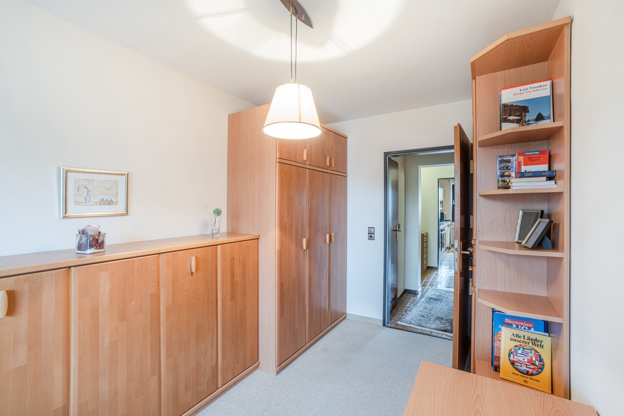 Kleines Zimmer mit Holzschränken, Regal mit Büchern und Deckenlampe.