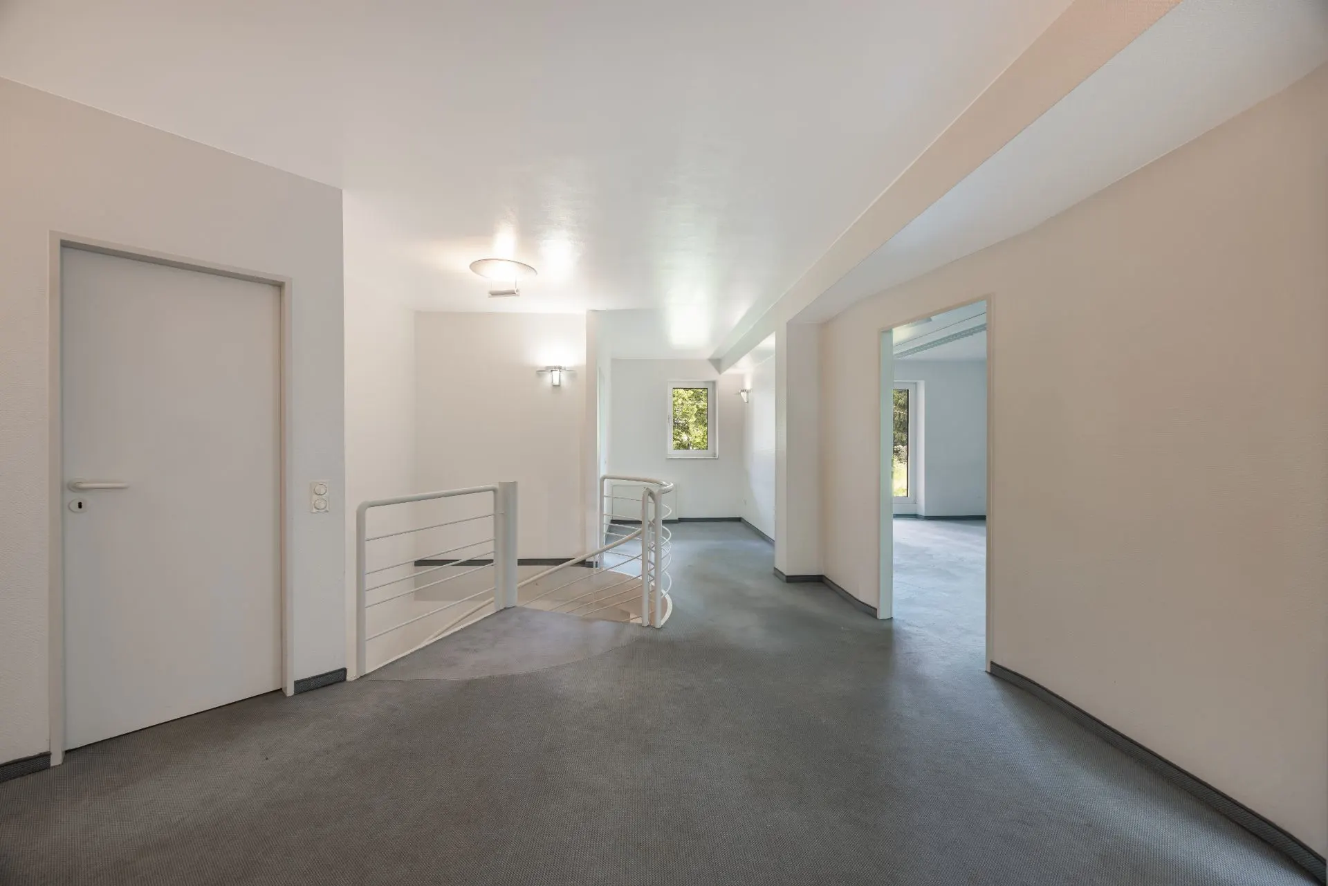 Heller Flur mit Tür, Geländer und Fenster, Zugang zu weiteren Räumen.