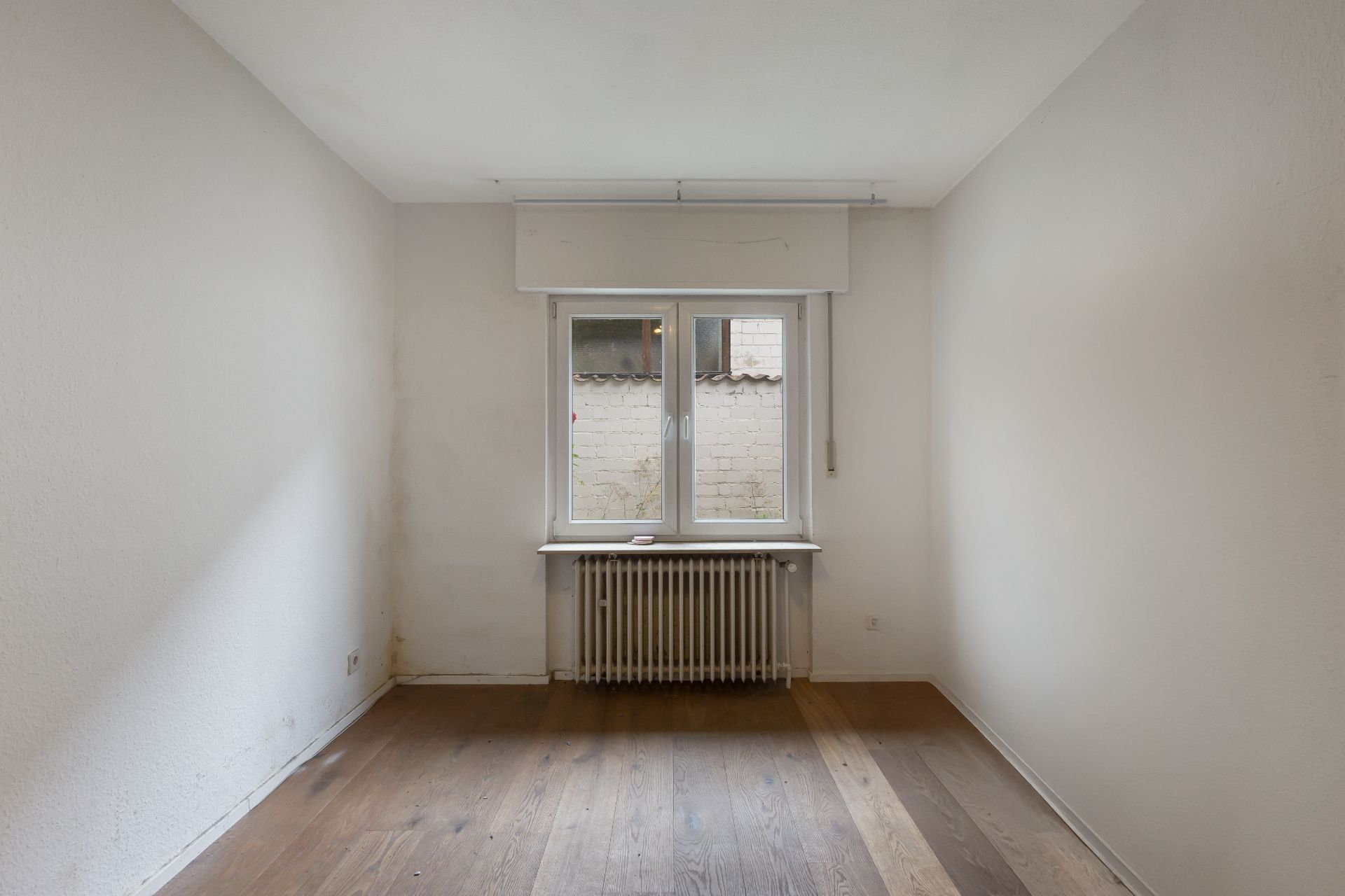 Leerer Raum mit Holzboden, Fenster und Heizkörper unter dem Fenster.