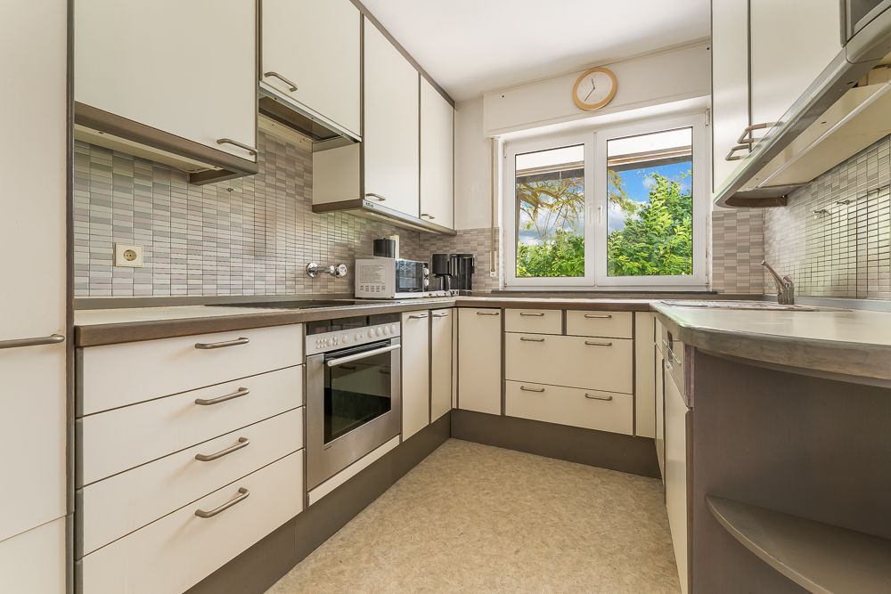 Moderne Einbauküche mit hellen Schränken, großem Fenster und Elektrogeräten.
