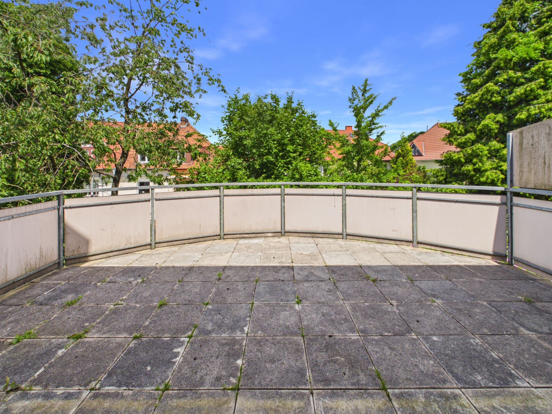 Große geflieste Terrasse mit Metallgeländer und Blick auf Bäume und Nachbarhäuser.