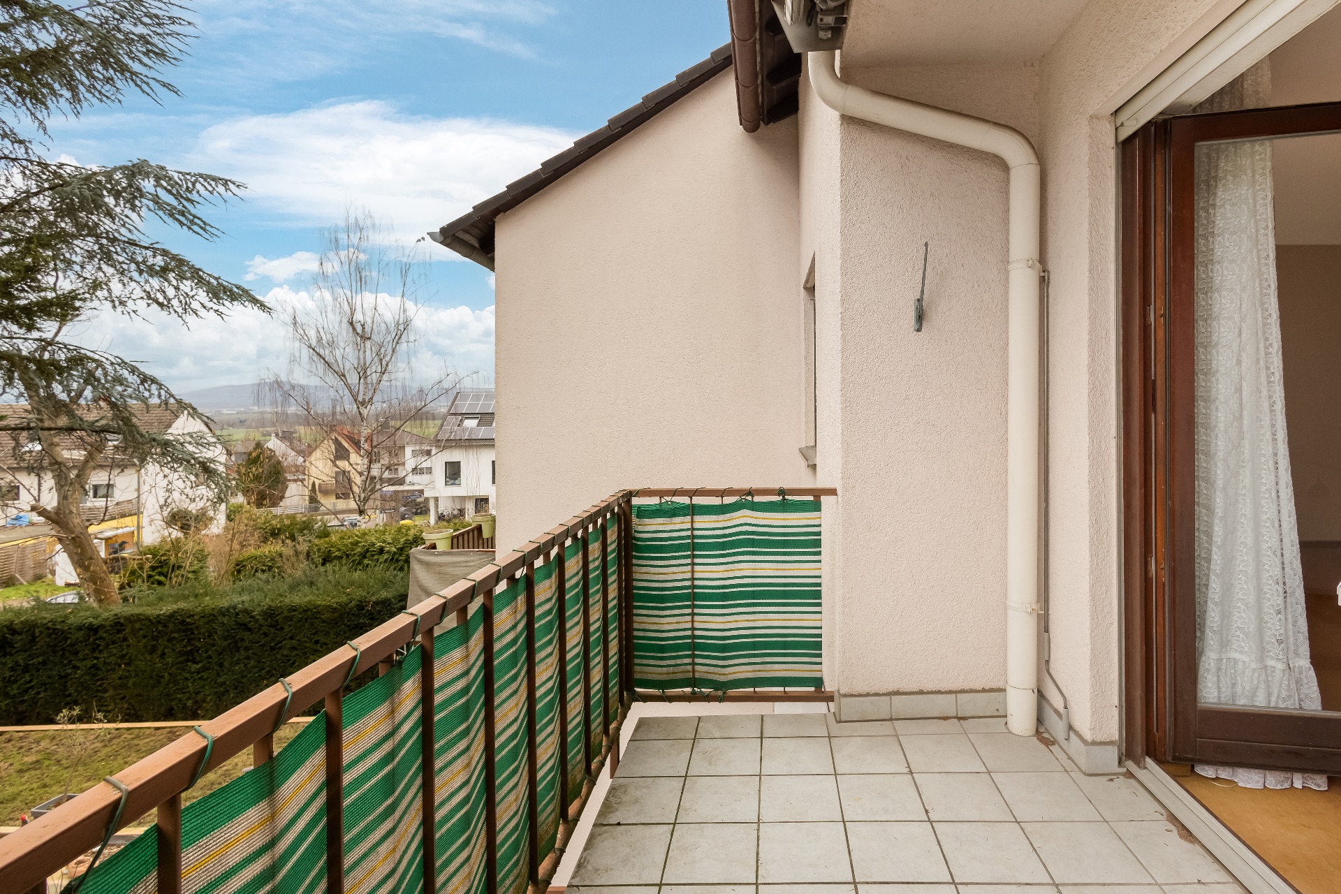 Kleiner Balkon mit Fliesenboden und grünem Sichtschutz, angrenzend an ein Wohnhaus.