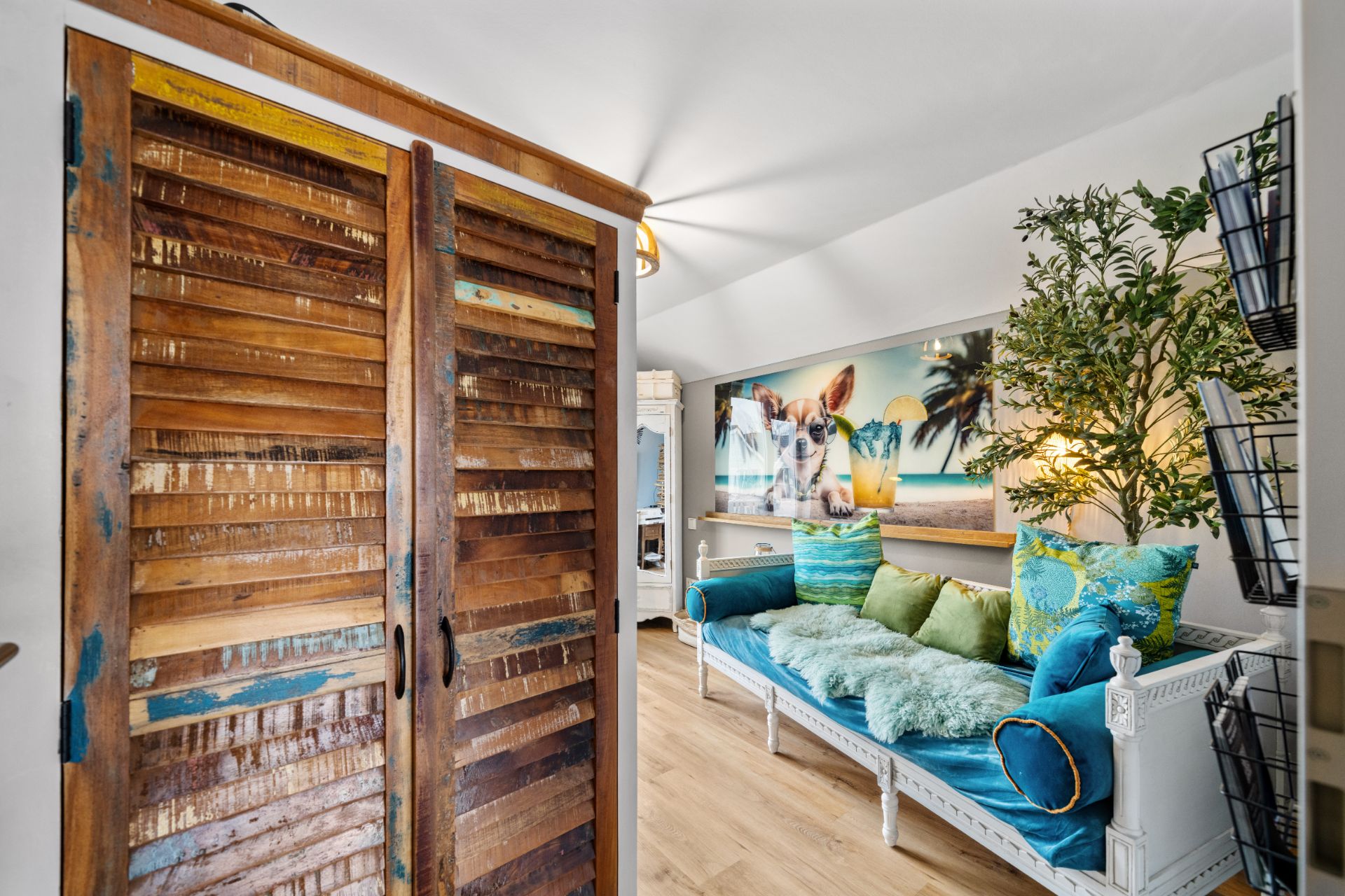Wohnzimmer mit bunter Couch, Holzboden, großem Bild an der Wand und Pflanze in der Ecke.