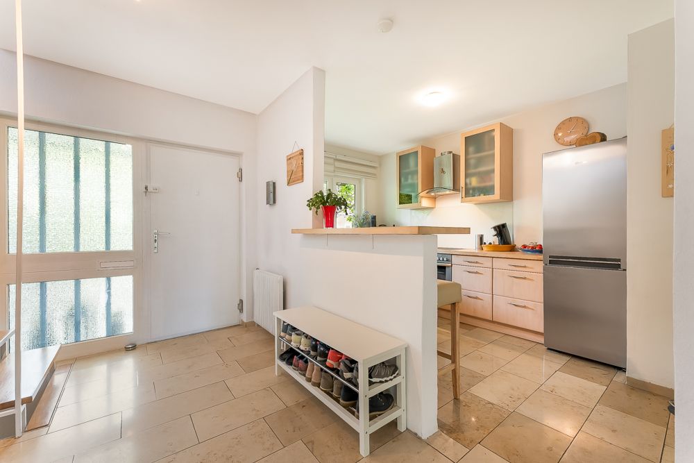 Heller Eingangsbereich mit Schuhregal und Blick in eine offene Küche mit großem Kühlschrank.