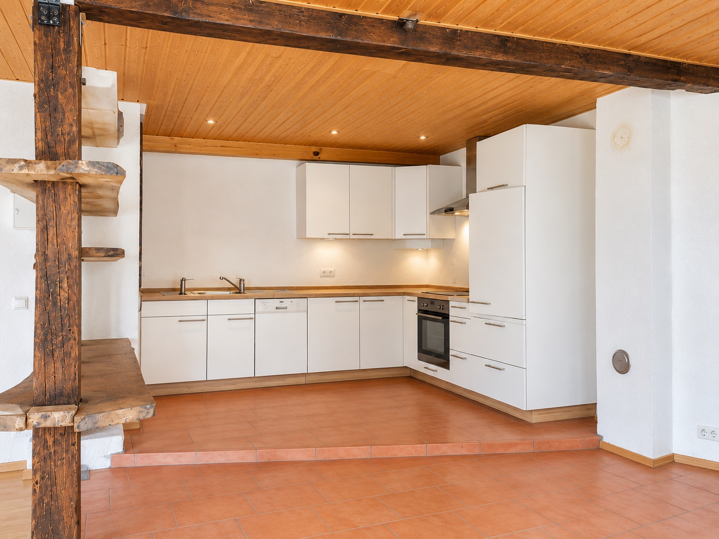 Helle Einbauküche mit weißen Schränken, Holzdecke und offener Holztreppe in einem Wohnraum.