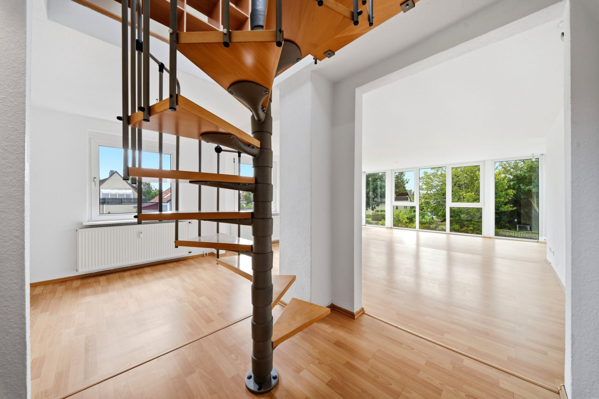 Wohnraum mit Holztreppe und großen Fenstern, heller Raum mit Parkettboden.