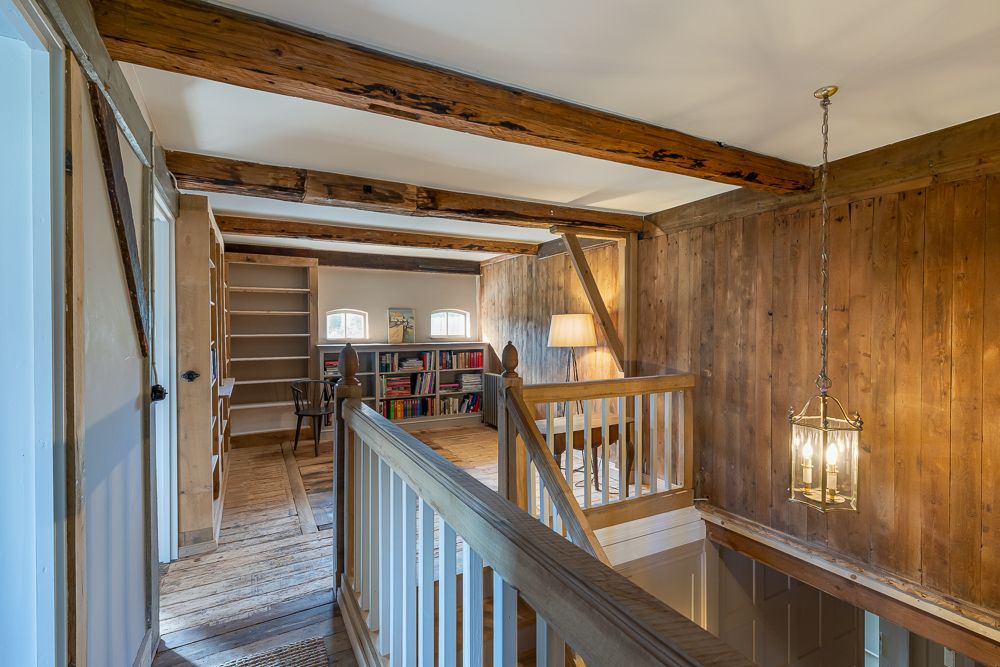 Heller Flur mit Holzwänden, Bücherregal, Stuhl und Stehlampe im Obergeschoss.