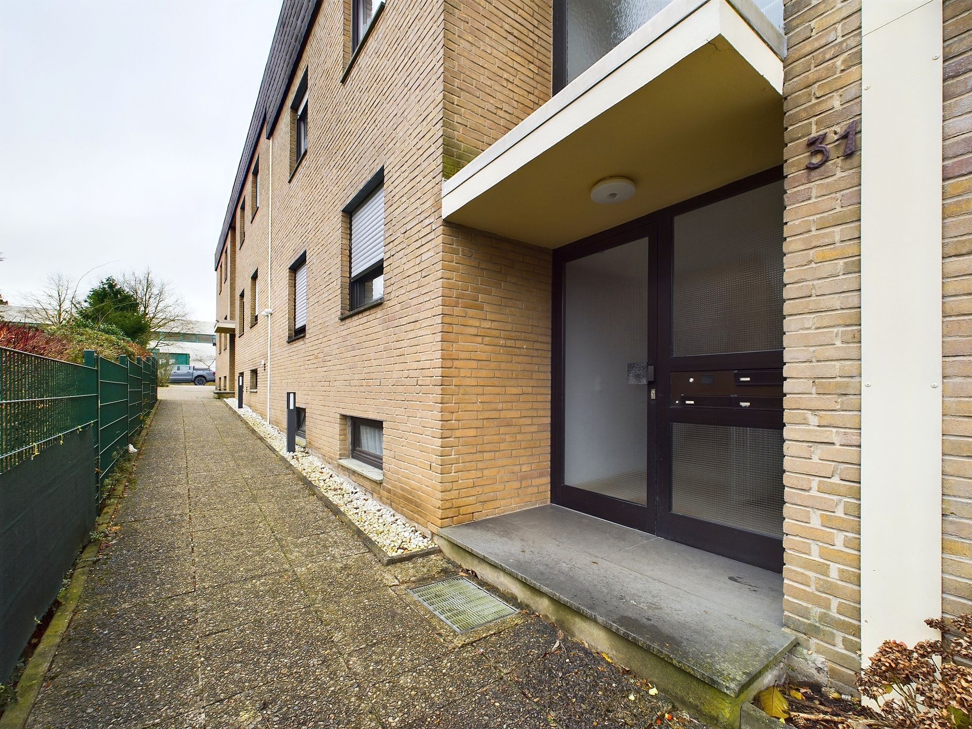 Eingang eines Mehrfamilienhauses mit brauner Klinkerfassade und Gehweg daneben.