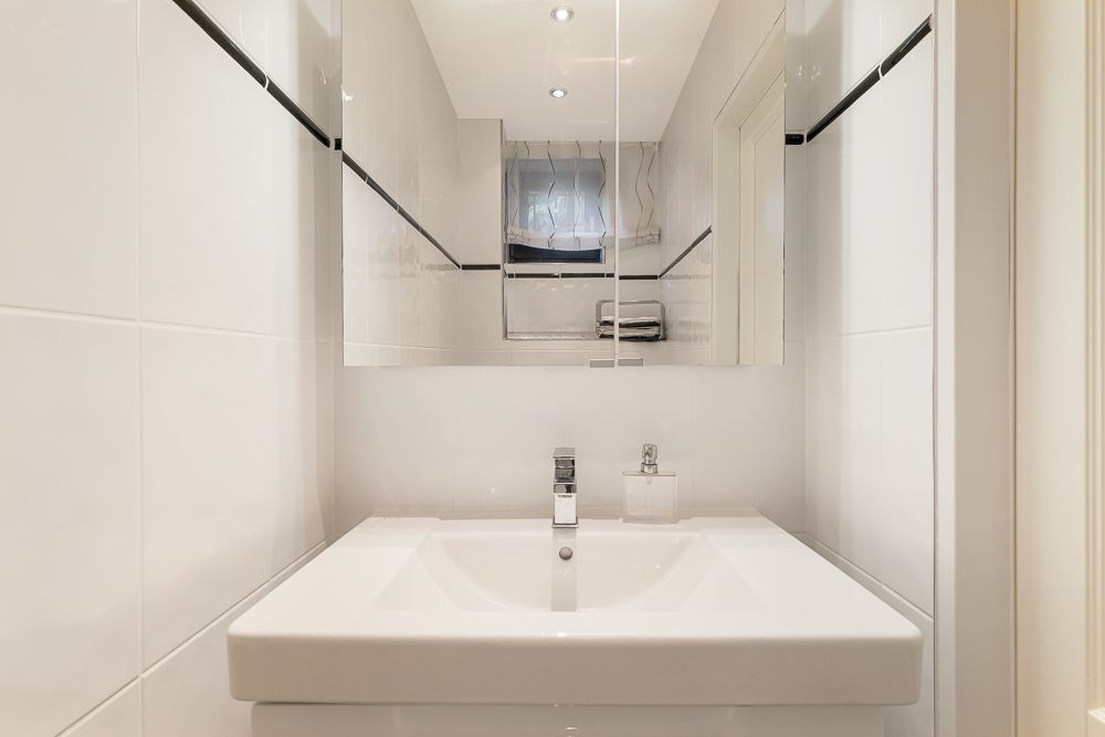 Modernes, weiß gefliestes Badezimmer mit Waschbecken und Spiegel.