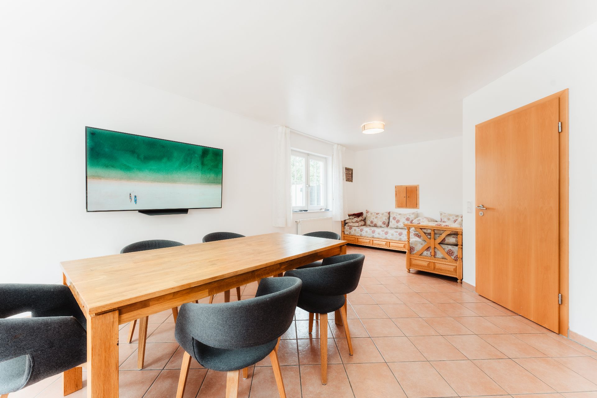 Essbereich mit Holztisch, sechs Stühlen, Sofa und Wandbild in hellem Raum.
