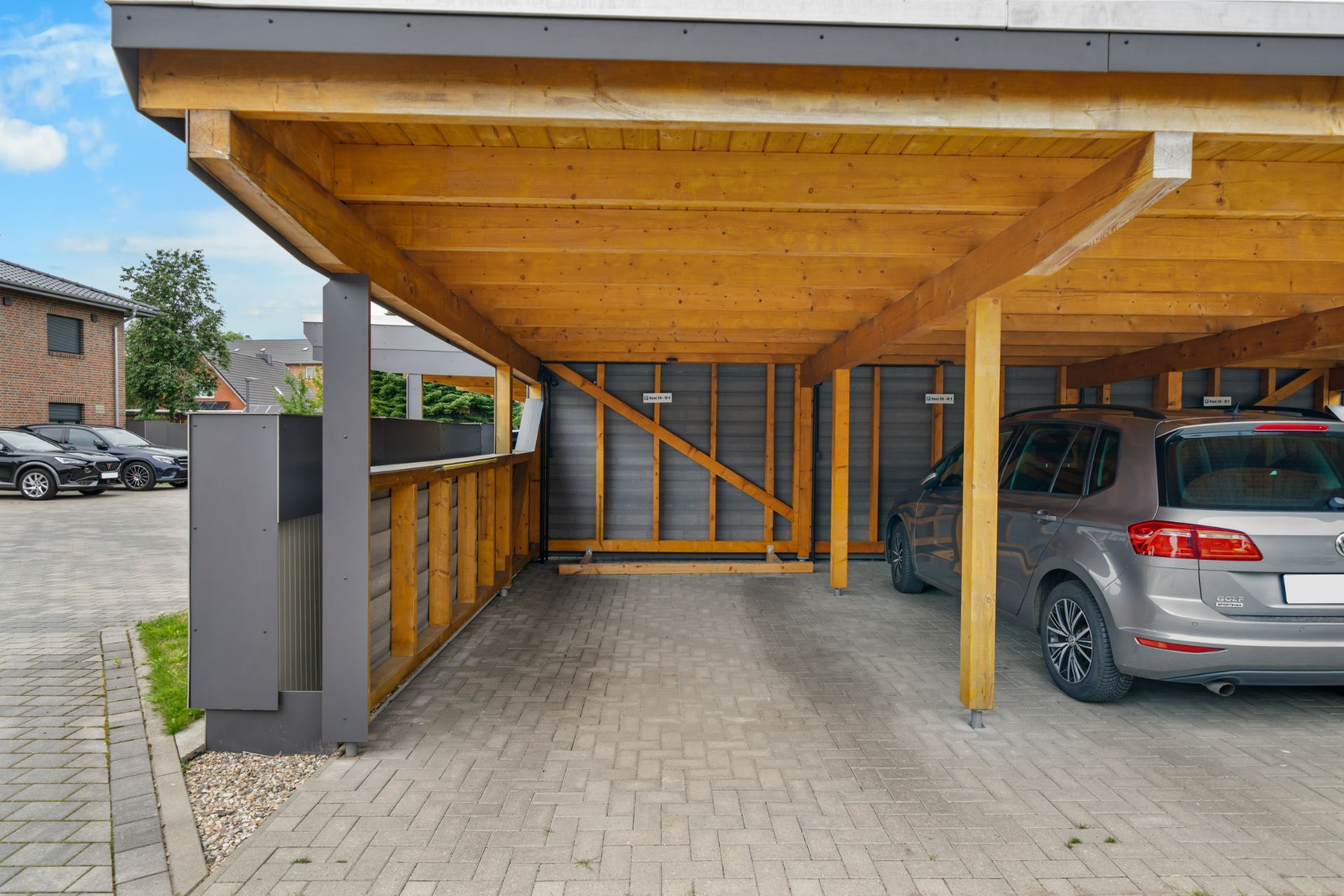 Holz-Carport mit zwei Stellplätzen, ein Auto parkt rechts, der linke Platz ist leer.